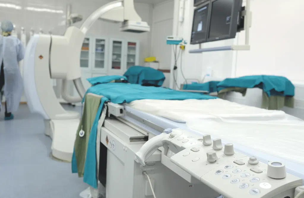 A medical imaging room with a patient table covered in green sheets.