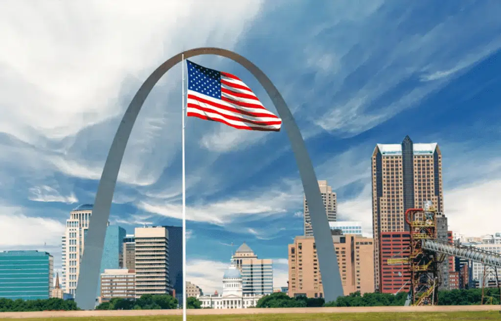 The Gateway Arch, a towering stainless steel monument in St. Louis, Missouri, with a large American flag waving in the foreground.